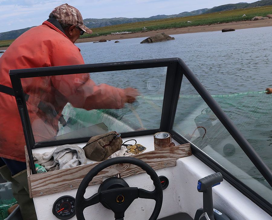 Innu man casting fishing net from boat