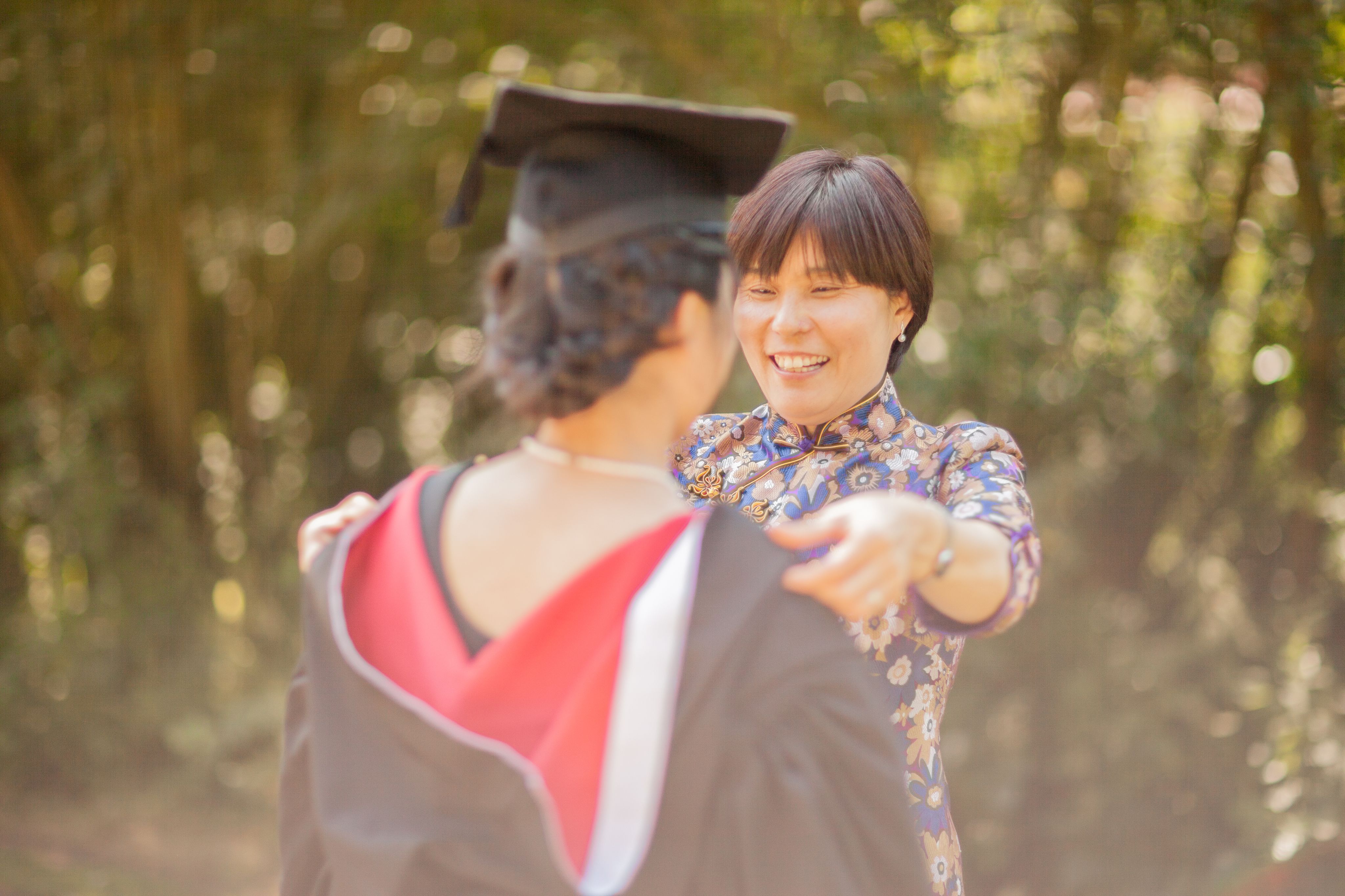 A woman, smiling, adjusts a graduate's academic gown