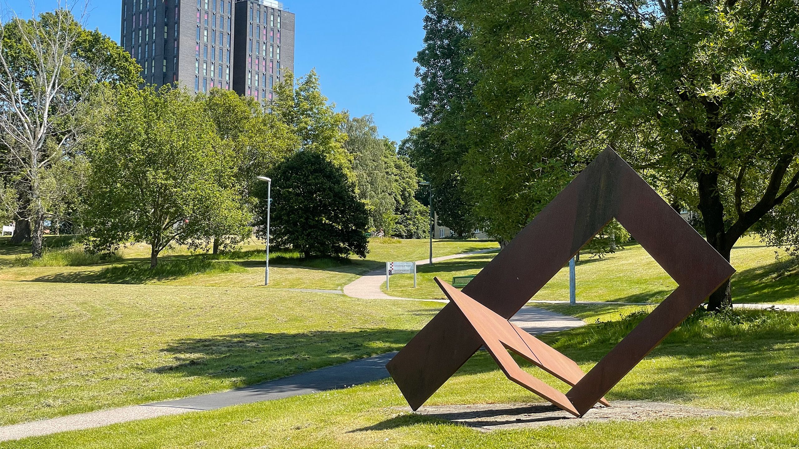 An angular steel ribbon twists about itself in front of one of Colchester Campus' towers.