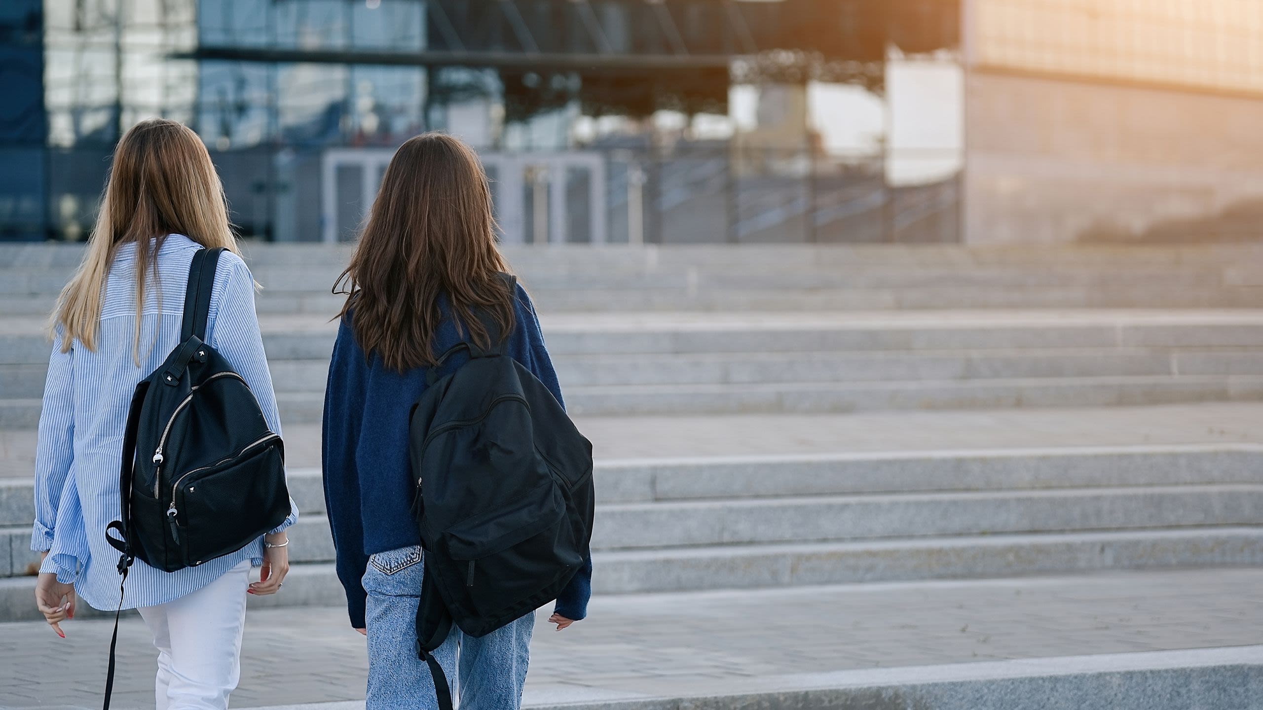 Two teenage girls, carrying rucksacks, walking across an open square, with their backs to the camera