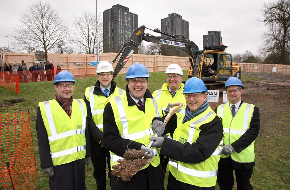 Registrar and Secretary Bryn Morris poses with other staff and a loaded shovel while dressed in a high-visibility jacket and hard hat.