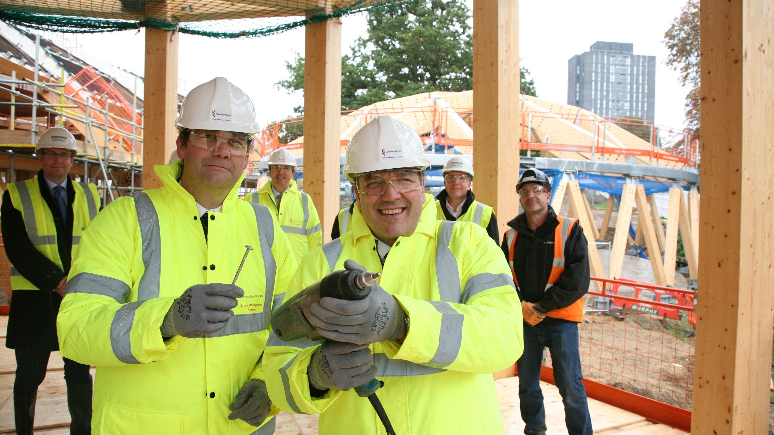 Registrar and Secretary Bryn Morris poses with other staff and a drill while dressed in a high-visibility jacket and hard hat.