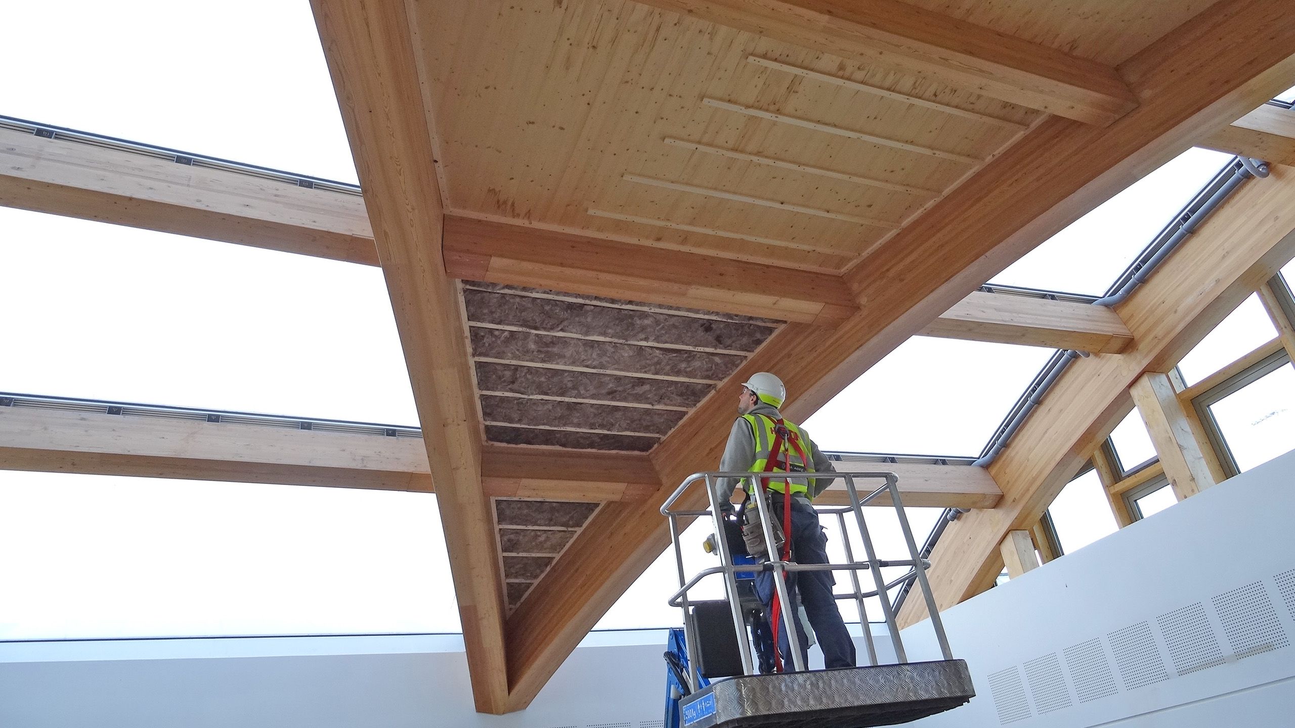 A construction worker is lifted to an incomplete roof by a cherry picker.