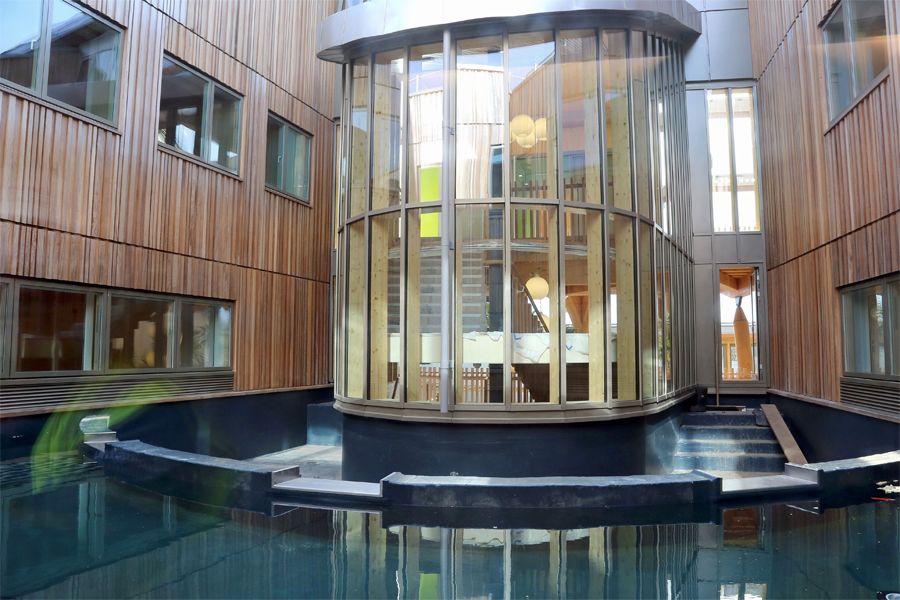 A glass stairwell juts out from a wooden-walled courtyard. The floor is a water-filled pool.