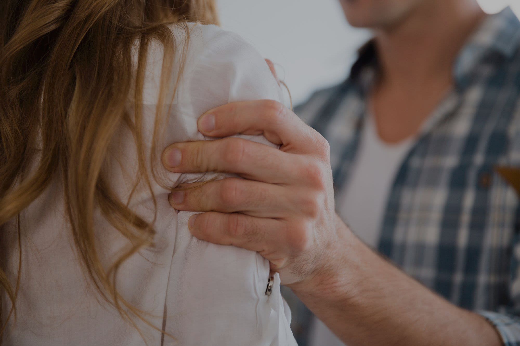 Image of a hand grabbing a female shoulder to demonstrate an example of domestic violence